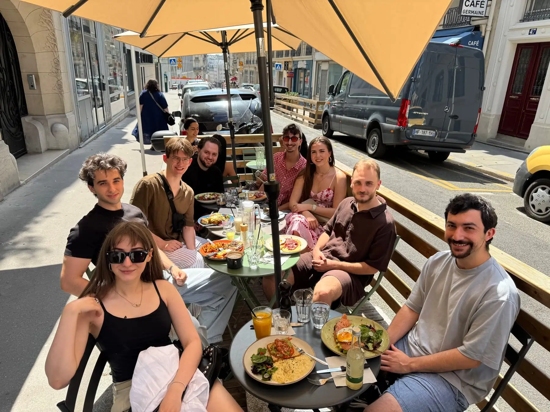 Team members at lunch around café tables on a sunny street.