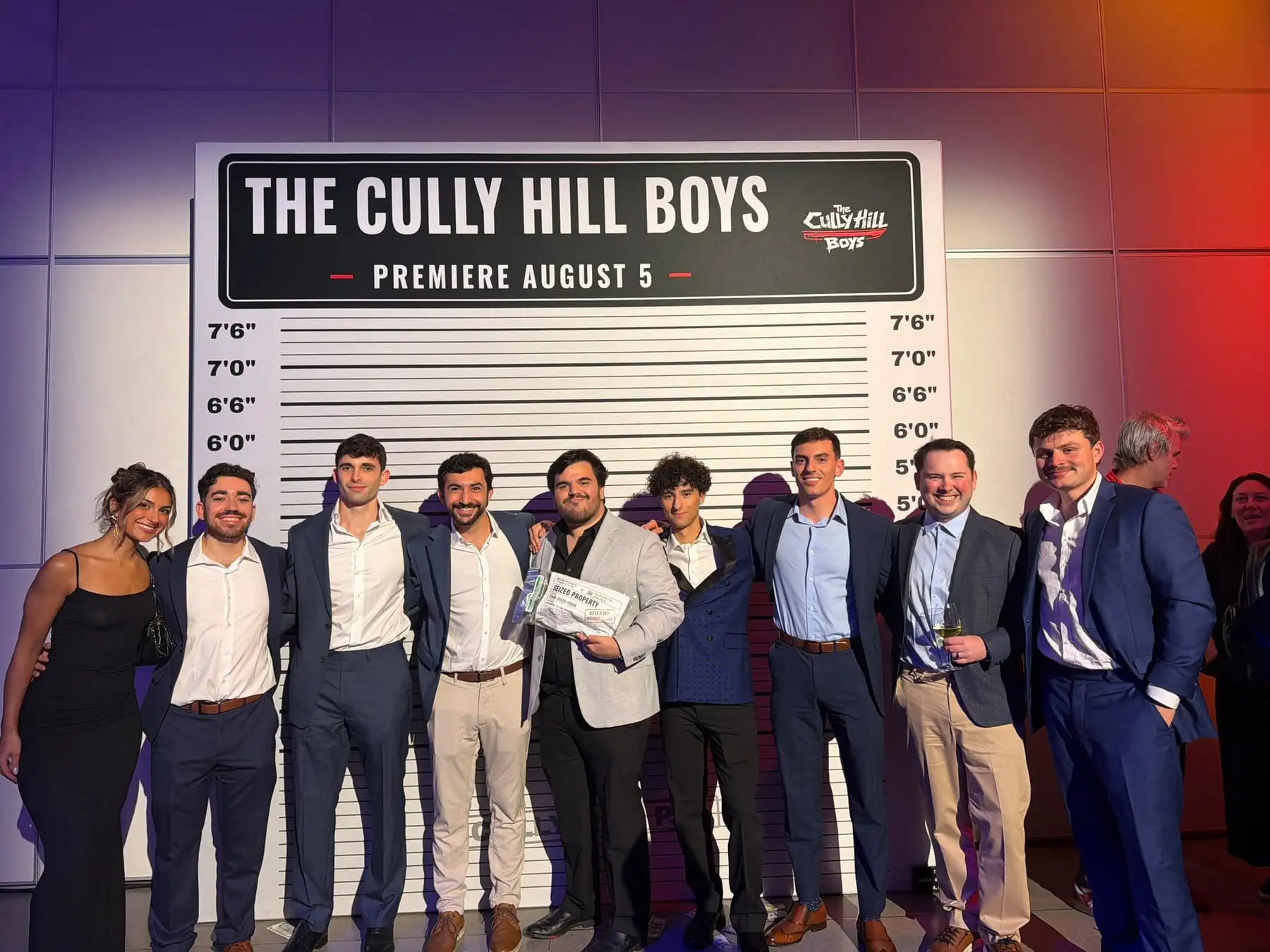 Team members in suits lined up in front of a height-chart backdrop that reads “The Cully Hill Boys, premiere August 5”.