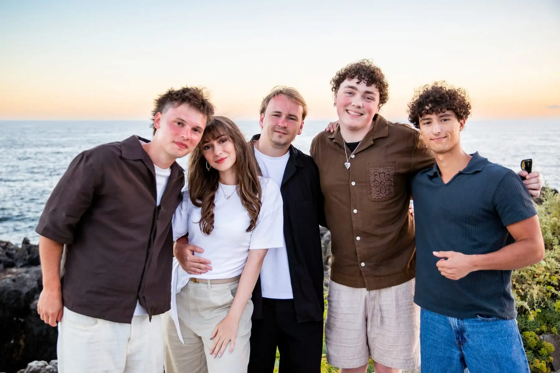 Five team members with their arms around each other in front of the sea at sunset.